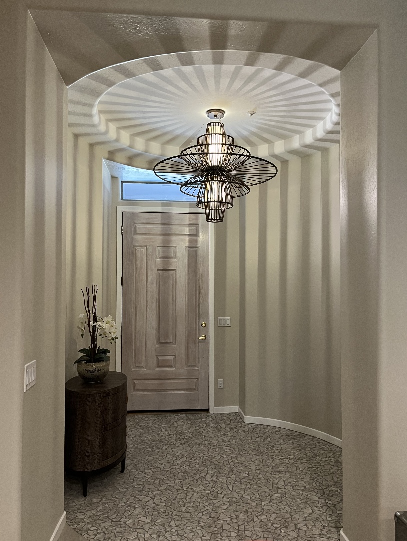 The front entryway to a home with the overlight lighting fixture casting a dramatic light and shadow striped pattern over the room.