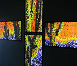 Four backlit panels showing a pixelated scene of saguaro cacti on a mountainous sunset background.